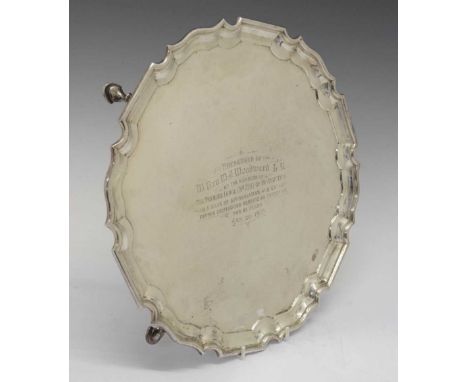 George V silver shaped circular salver with piecrust border standing on four hooved feet with Masonic inscription 'Presented 