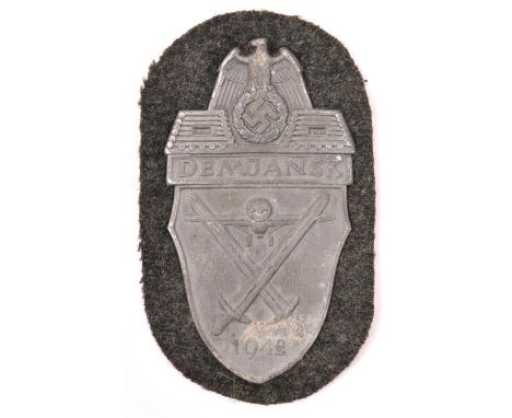 A Third Reich Demjansk shield, of grey zinc on field grey patch with original paper backing. Unissued Condition. 