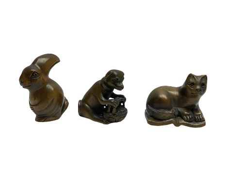 Three netsuke, modelled as a rabbit, dog with a basket and cat sat upon an open book
