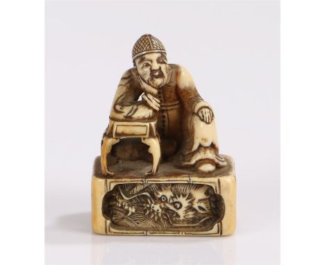 Japanese Edo period ivory tobovi netsuke depicting a scholar seated at a table with his head resting on his hand, a coiled dr