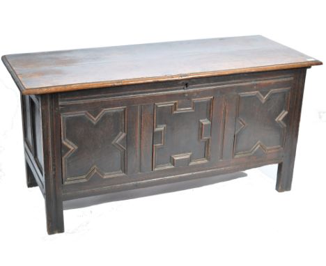 An 18th century carved oak coffer chest raised on bracket feet having a series of fielded geometric pattern panels with hinge