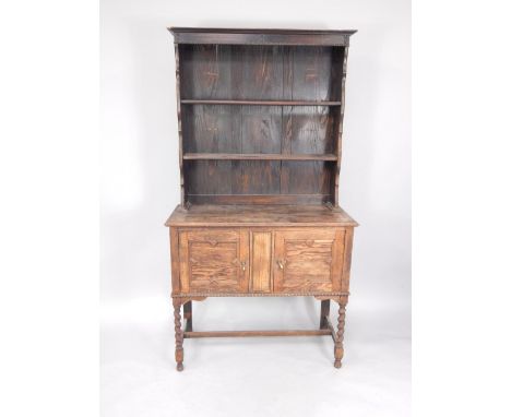 An early 20thC oak dresser, the two shelf delft rack, over a pair of panelled doors, raised on barleytwist supports united by