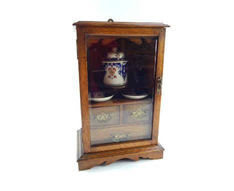 A Victorian oak smoker's cabinet, the glazed door opening to reveal a shelf and three drawers, with a jar and two dishes, rai