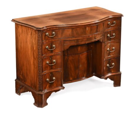 An Edwardian George III style mahogany serpentine fronted desk, with plate glass top and rear hinged flap with serpentine fro