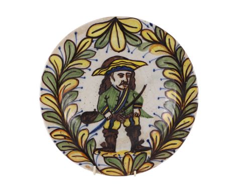 A maiolica style tin glazed earthenware plate with central figure within a foliage border, 29cms wide.