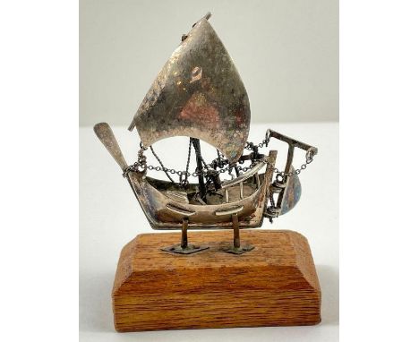 A silver model of a Chinese 'junk' boat, with articulated rudder, 6.7cm high, on a related wooden base, 17.49g gross, unmarke
