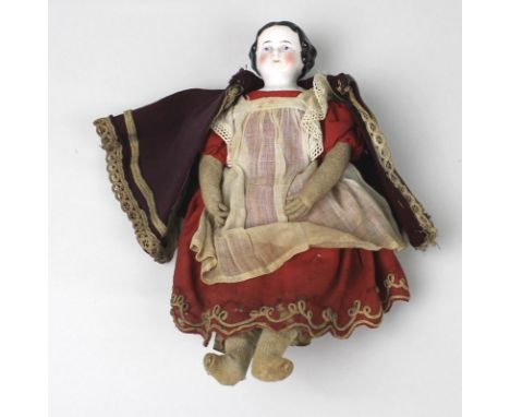 A 19th century doll with painted porcelain head, straw stuffed body, wearing a red dress, a white pinafore and a burgundy col