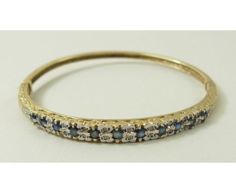 A 9ct gold bangle, half set with eleven sapphires divided by ten pairs of diamonds and flanked by two single diamonds, within