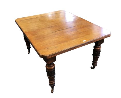 An Edwardian walnut wind out dining table, the rectangular top with canted corners raised on foliate carved pillar legs and c
