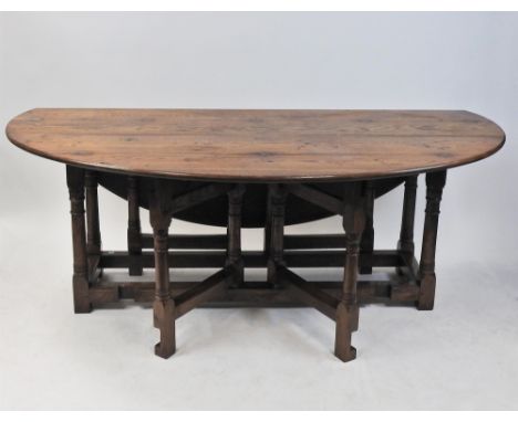 An oak double gate leg action dining table, the oval twin flap top raised on pilaster and block legs, joined by heavy grooved
