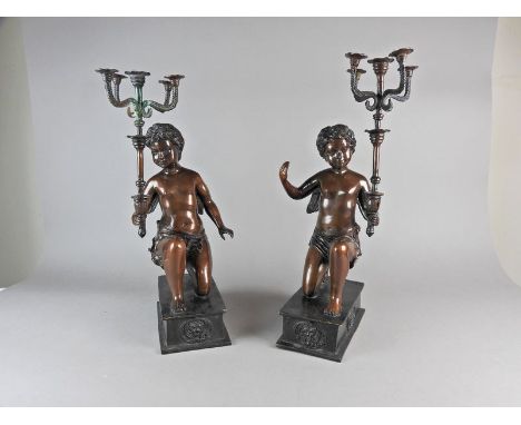 A pair of bronzed metal figural candelabra, 20th century, each cast as a kneeling cherub holding a five-sconce torch on a rec