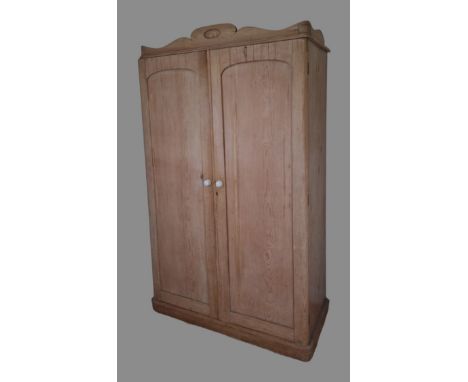 A pine wardrobe, the moulded cornice above two panel doors enclosing hanging space and drawers raised upon a plinth, 126cms w