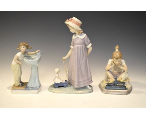 Three Lladro figures comprising: a girl with doll in pullalong cart, 27.5cm high, 4838 girl standing at a wash basin, and 547