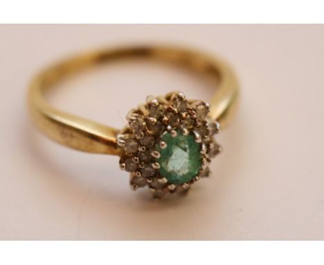 A ladies 9ct yellow gold ring set with a central oval cut emerald with diamond surround