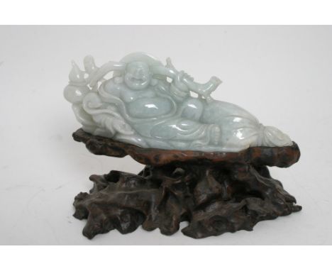 A carved hard stone jade reclining Buddha on a root wood base. 20 x 26 cm (including stand)