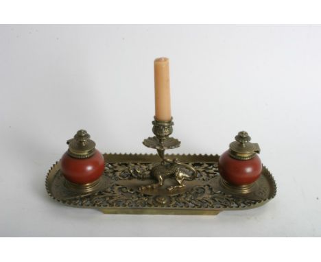 A ornate brass inkwell stand inset with a candlestick formed as a mythical creature