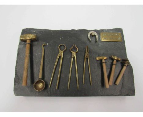 A miniature set of blacksmith's tools on a slate plinth