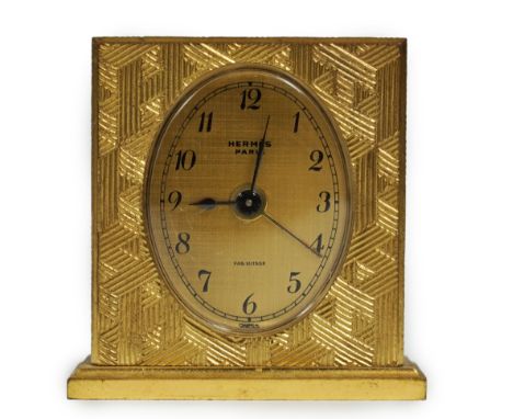 A Hermès travel alarm clock in gilded brass chiselled with H enchassés, in original leather case, dial signed “Hermès Paris",