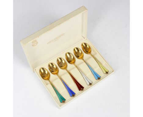 A cased set of six enamelled silver gilt teaspoons, the tapered stems with shaped terminals in various enamelled colours, sta