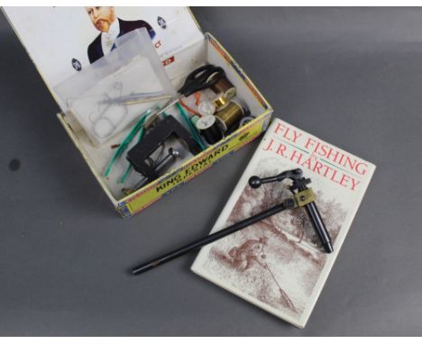 A fly tying vice, together with various tools and a copy of "Fly Fishing" by JR Hartley.
