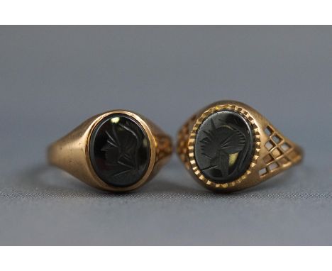 A selection of two yellow gold signet rings each set with a carved hematite intaglio. Both hallmarked 9ct gold. Sizes P & R. 