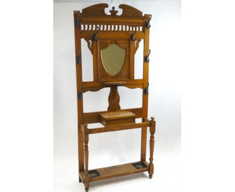 An early 20th century oak hallstand with central shield shape mirror over a bracket shelf, lidded box and stickstand base, 21
