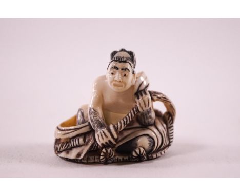 An early 20th century Japanese ivory netsuke, carved as a seated man holding a rope, signed to the base, 3.5cm high