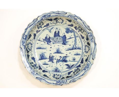 A substantial Chinese porcelain blue and white dish with shaped edge, the central panel depicting three figures playing chess