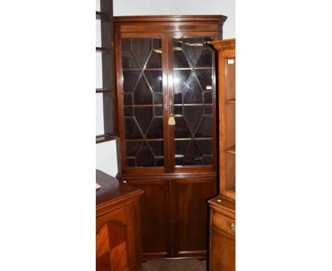 A late George III mahogany floor standing corner cupboard, with a moulded cornice over an astragal glazed two door upper sect