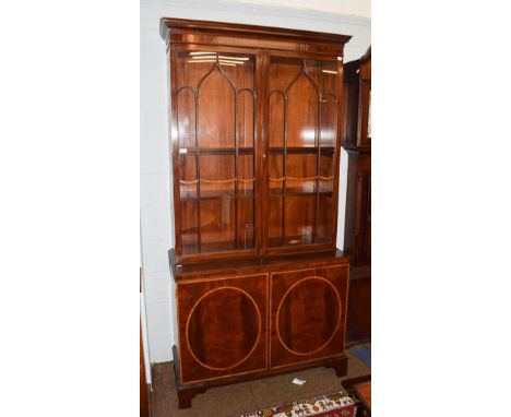 A Georgian style mahogany and satinwood banded bookcase, moulded cornice above twin glazed doors, base with twin cupboard doo
