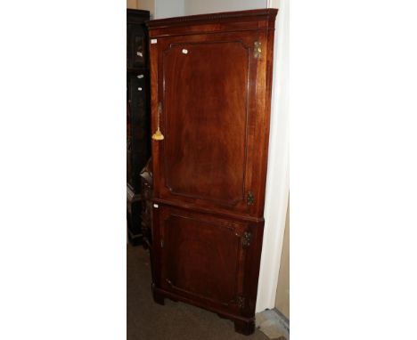 A Georgian style mahogany full-height corner cupboard, integral dentil moulded cornice above two panelled doors, bracket supp