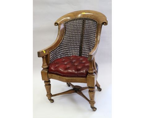 A child's early 19th century cane back scroll armchair with seat button upholstered in a leather, on turned and stretchered