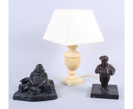 A brass inkwell, in the form of a seated man, a cast iron model of a man and a stone table lamp