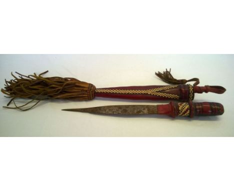 A vintage tribal dagger with a red leather handle and scabbard decorated with woven straw checkeboard design and leather tass