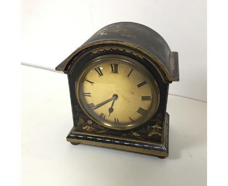 A 1920s lacquered mantel clock with chinoiserie decoration, with arched top over a metal dial with Roman numerals, on bun fee