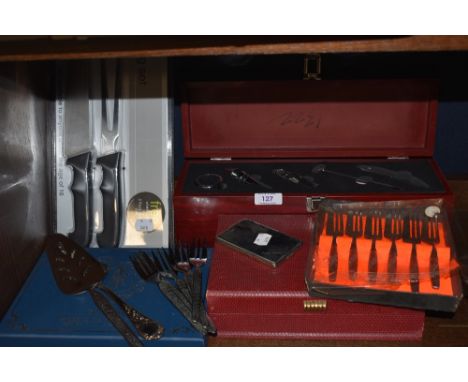 An assortment of flat ware including boxed spoons and wine tools in display case.