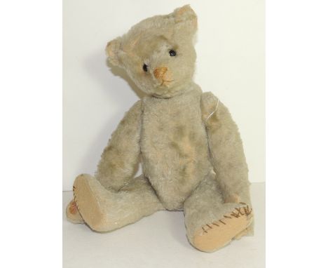 An early 20th Century teddy bear with light plush covering and having black boot button eyes, pronounced snout with brown sti