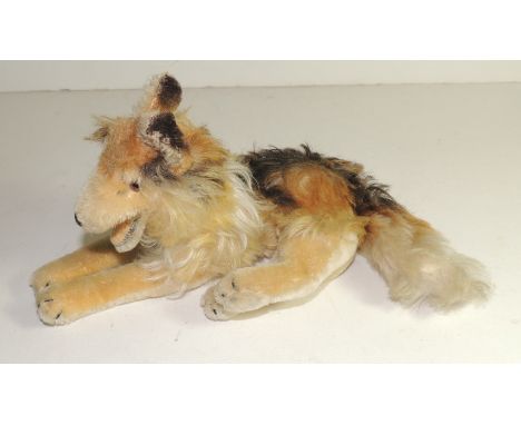 A Steiff toy German Shepherd type dog, lying down, with printed plush, open mouth, glass eyes and stitched claw detail, c.196