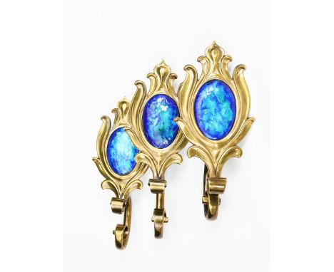 Three enamelled brass curtain ties,  each cast as a stylised flower stem, set with vivid blue enamel panel, unsigned, 22cm. w