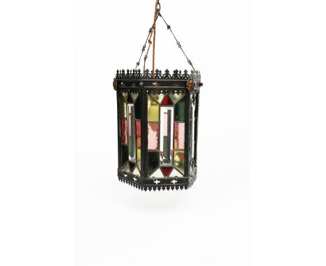 A patinated metal hall lantern, hexagonal section with pierced arch mantel border, set with coloured geometric glass panels, 