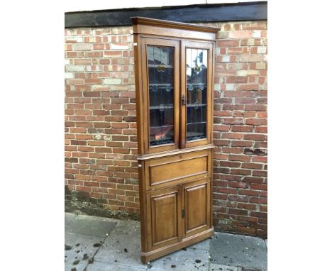 An early 20th century light oak standing corner cupboard in arts and crafts style with a pair of lead-glazed doors enclosing 