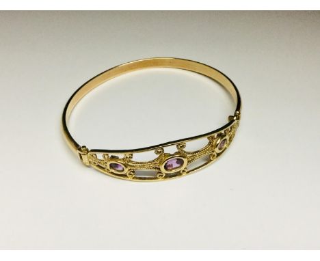 A 9ct yellow gold hinged bangle with 3 x oval rub over set Amethysts in a gold filigree top, weighing 8.6 grams. 