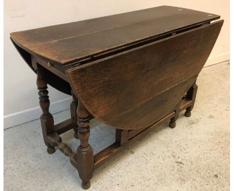 An 18th Century oak gate-leg drop-leaf dining table, the oval top on turned and block supports united by stretchers, 145 cm w