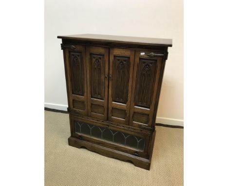 An Old Charm oak tv cabinet, the plain top over two folding arch panelled doors and leaded glazed fall front compartment rais