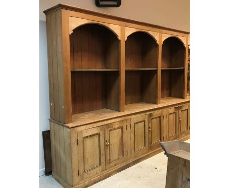 A circa 1900 pine dresser, the boarded three section upper shelf unit with arched decoration over three pairs of panelled cup