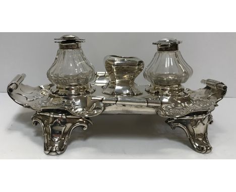 A Victorian silver desk stand, the cut glass inkwells flanking a central recess within a pierced decorative base with scroll 