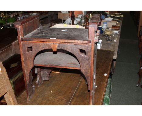 An Edwardian oak stool of ecclesiastical design, the seat with pegged construction over an arch with under shelf and pierced 