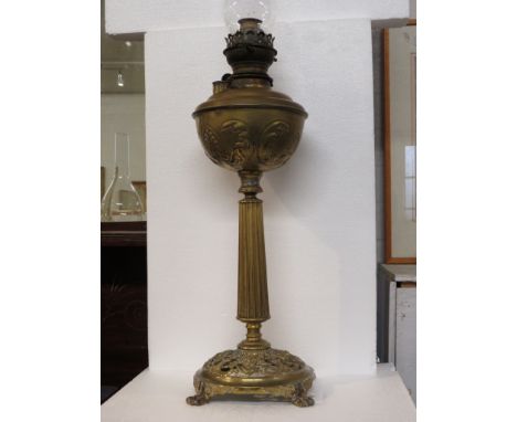 Brass oil lamp with embossed reservoir on a reeded tapering column with circular foot pierced and moulded with mask heads, st