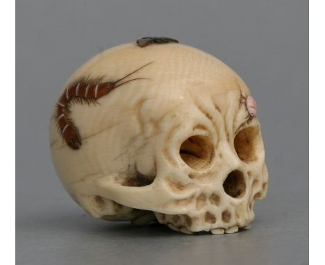 A Japanese ivory netsuke carved in the form of a skull with shibayama decoration, 3.5cms (1.25ins) wide.