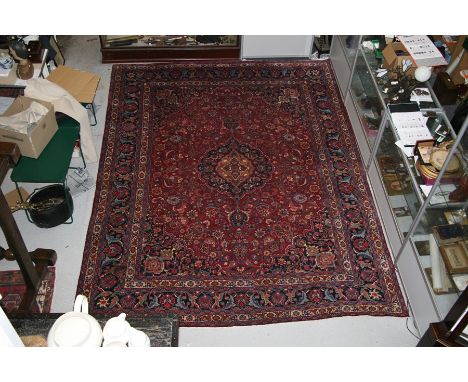 A Persian Kashan hand knotted woollen carpet with central floral gul within floral borders, on a red ground, 390 by 300cms (1